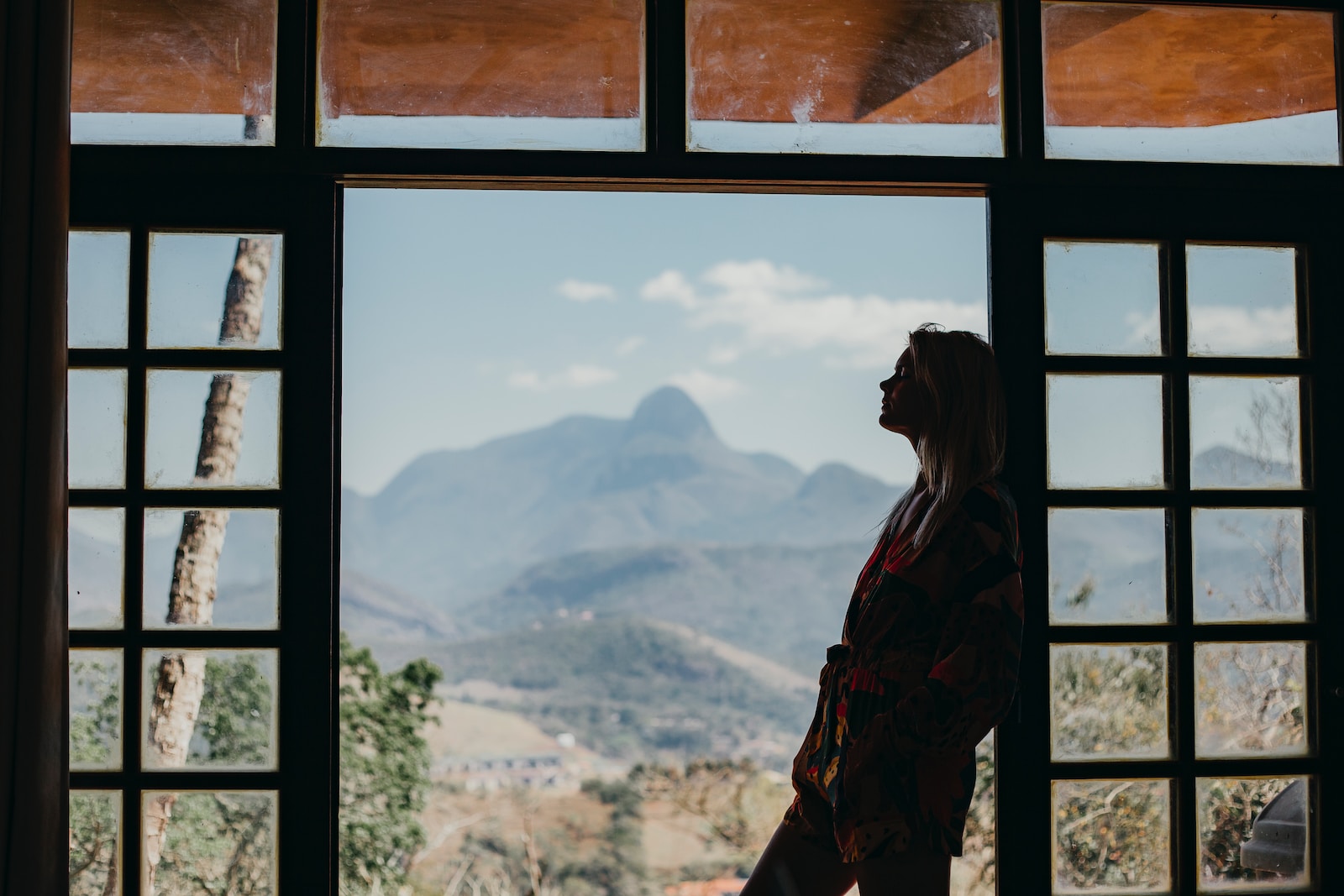 woman in red and black plaid dress shirt standing on window looking at mountains during daytime